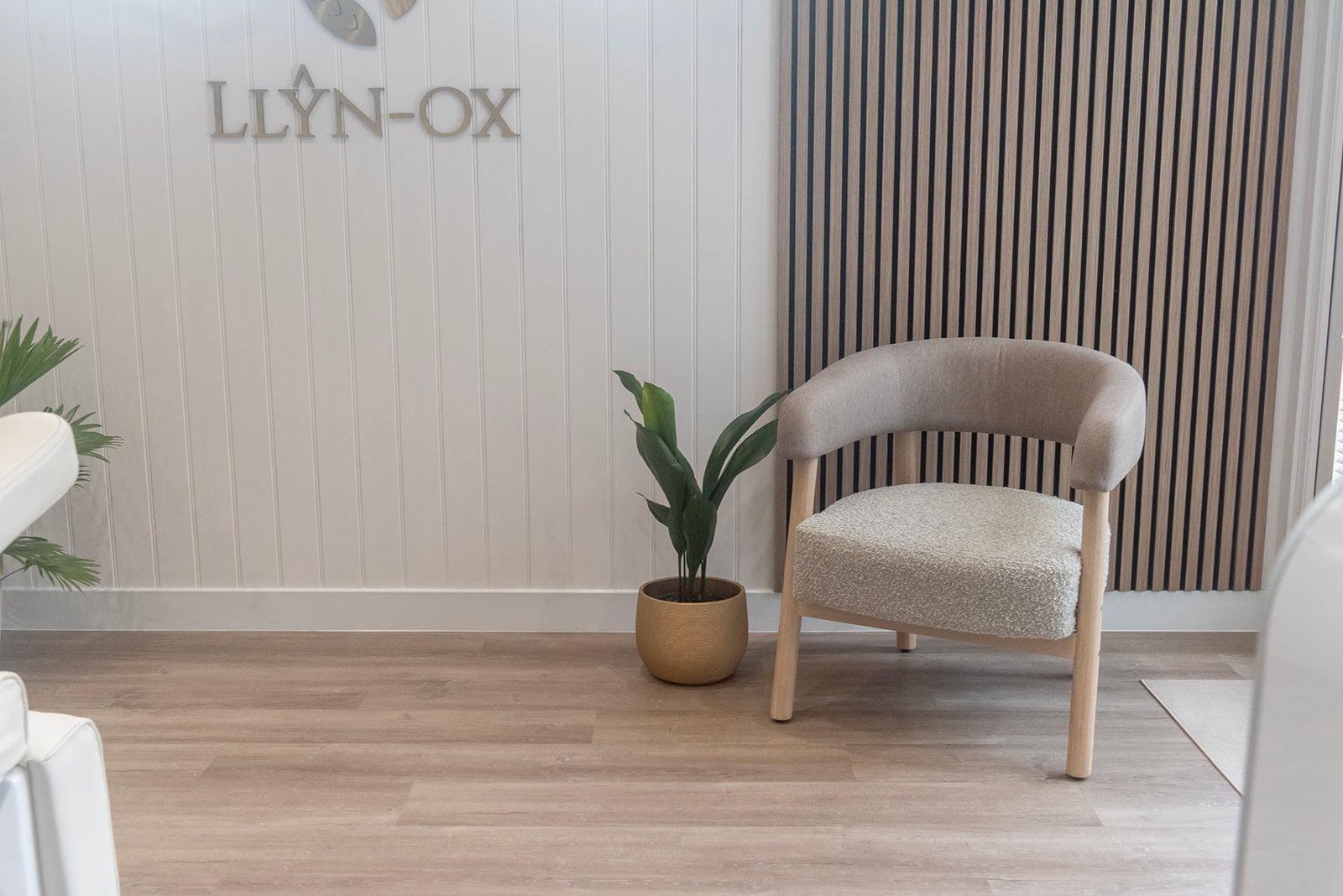 Beige armchair in a room with wooden flooring and a plant, featuring the brand 'LLYN-OX'.