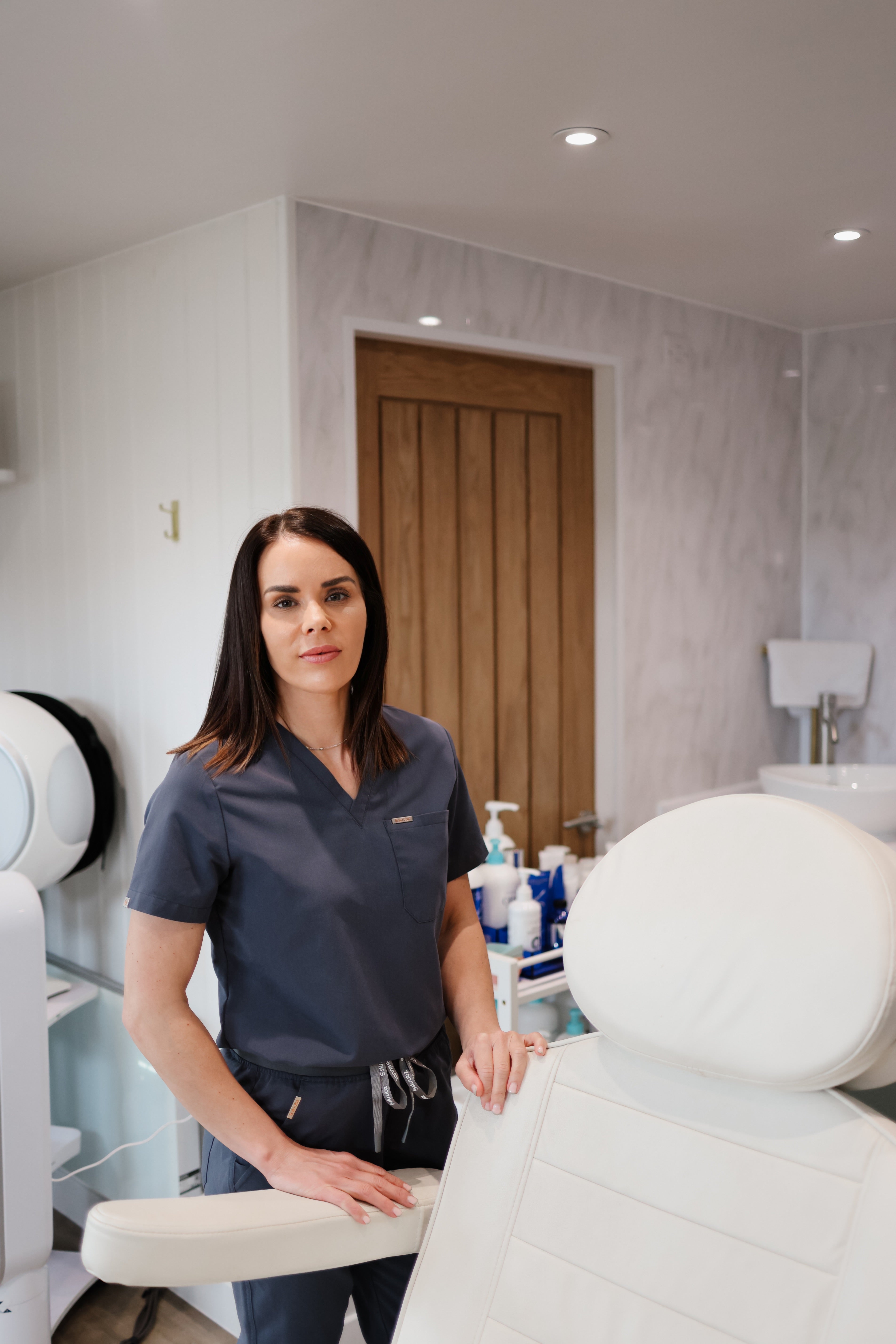Woman in an aesthetics salon standing next to a treatment chair.