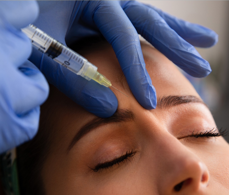 Person receiving a facial injection with blue gloves and a syringe.