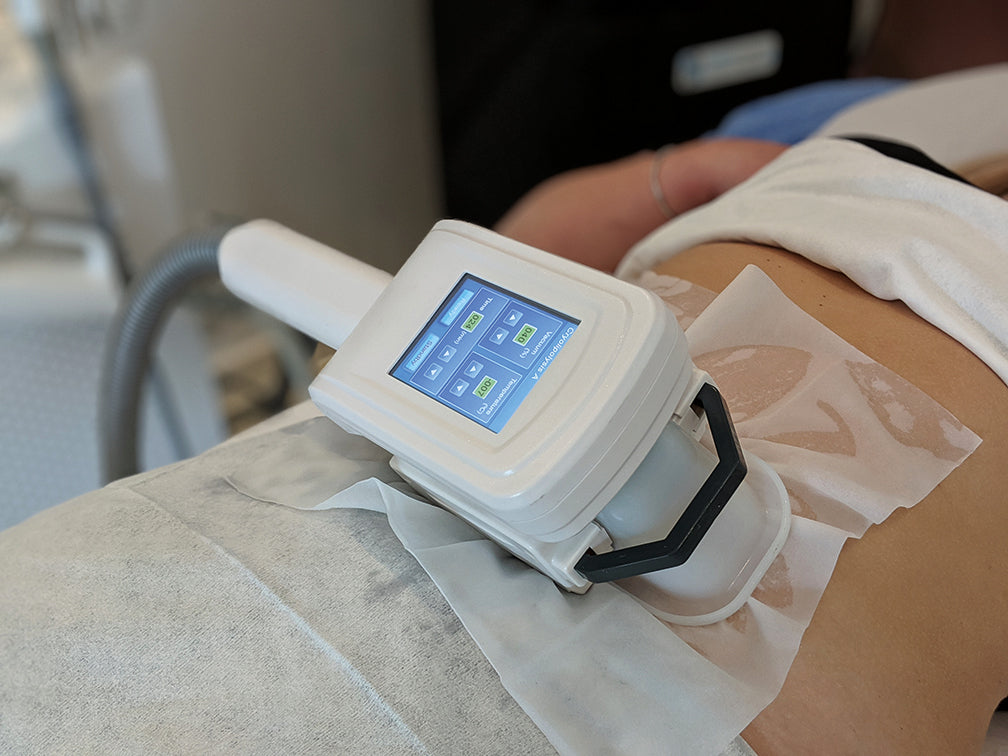 Medical device on a patient's stomach with a digital display, likely used for treatment.