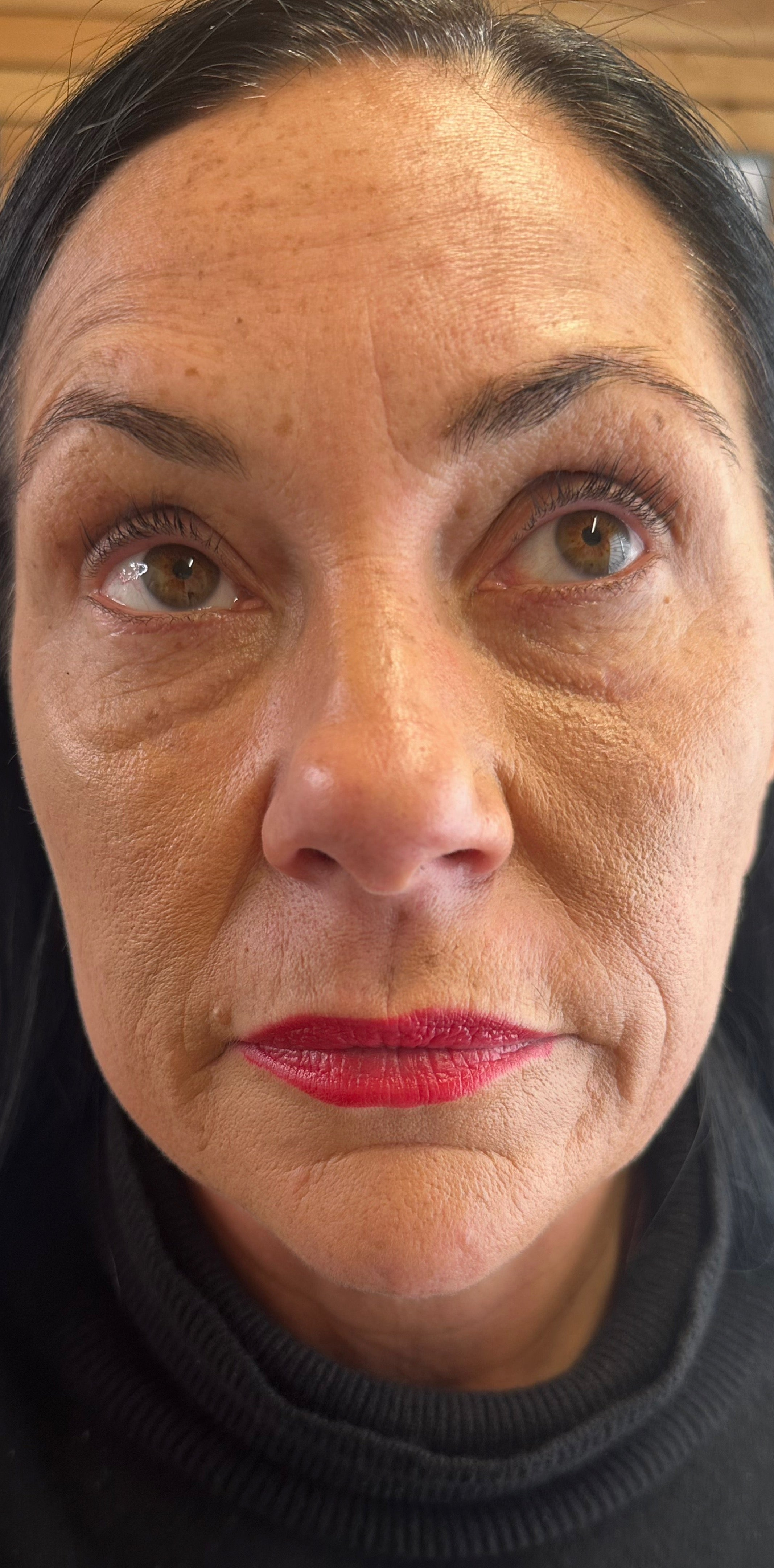 A close-up portrait of a woman's face showing her eyes, nose, and lips, wearing a black ribbed turtleneck sweater.